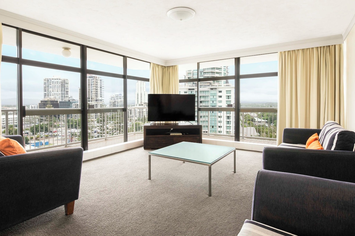 A modern living room with a flat-screen TV, a glass coffee table, and two sofas.