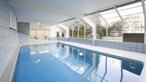 Piscina interior com água azul cristalina, rodeada por paredes brancas e grandes janelas.