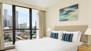 Quarto de hotel com uma cama grande, duas luminárias de cabeceira, vista para a cidade e um quadro na parede.