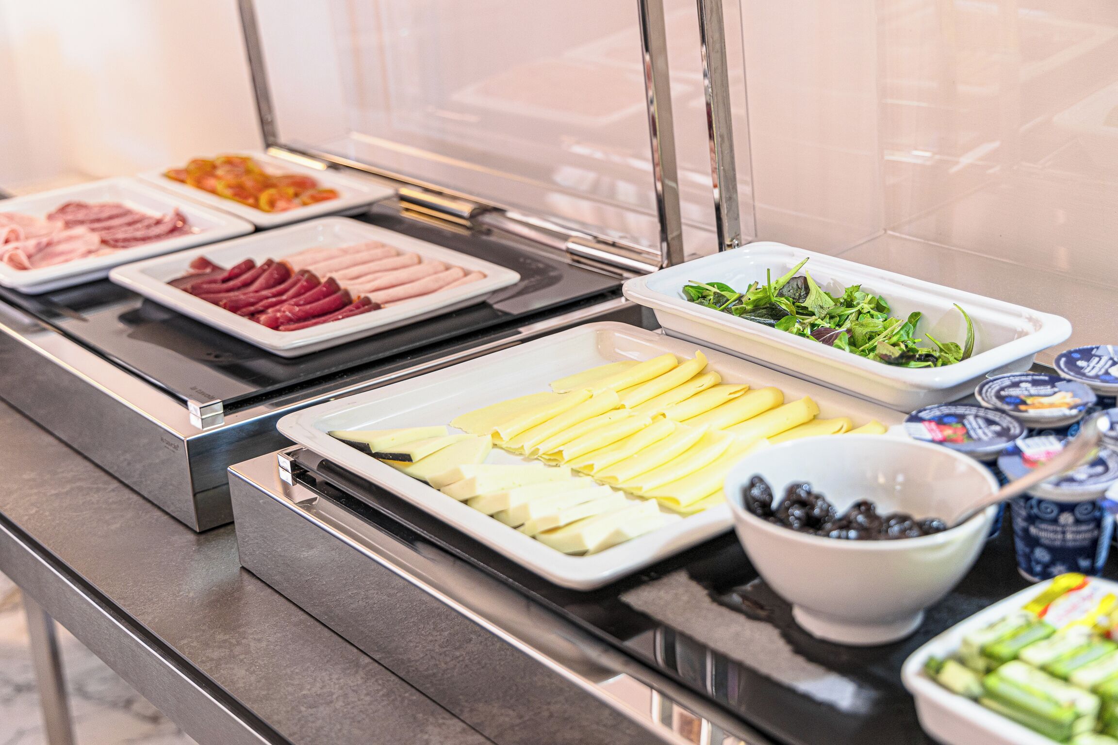 A buffet with various food items including sliced meats, cheeses, fruits, and salads.
