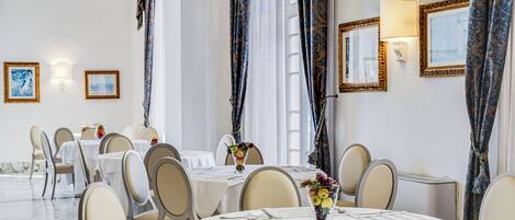 A dining area with round tables, chairs, and a vase of fruit on each table.