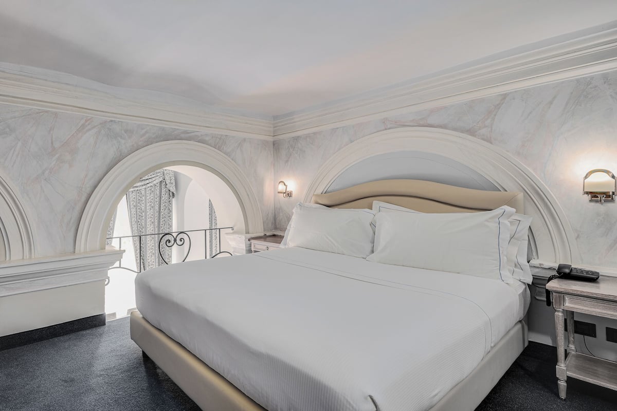 Een hotelkamer met een groot bed, marmeren wanden en uitzicht door een rondbogig raam.