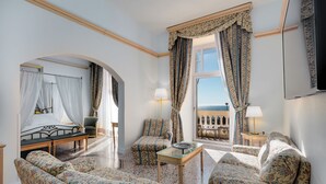 A hotel room with a bed, a sofa, a chair, a table, and a balcony with curtains.