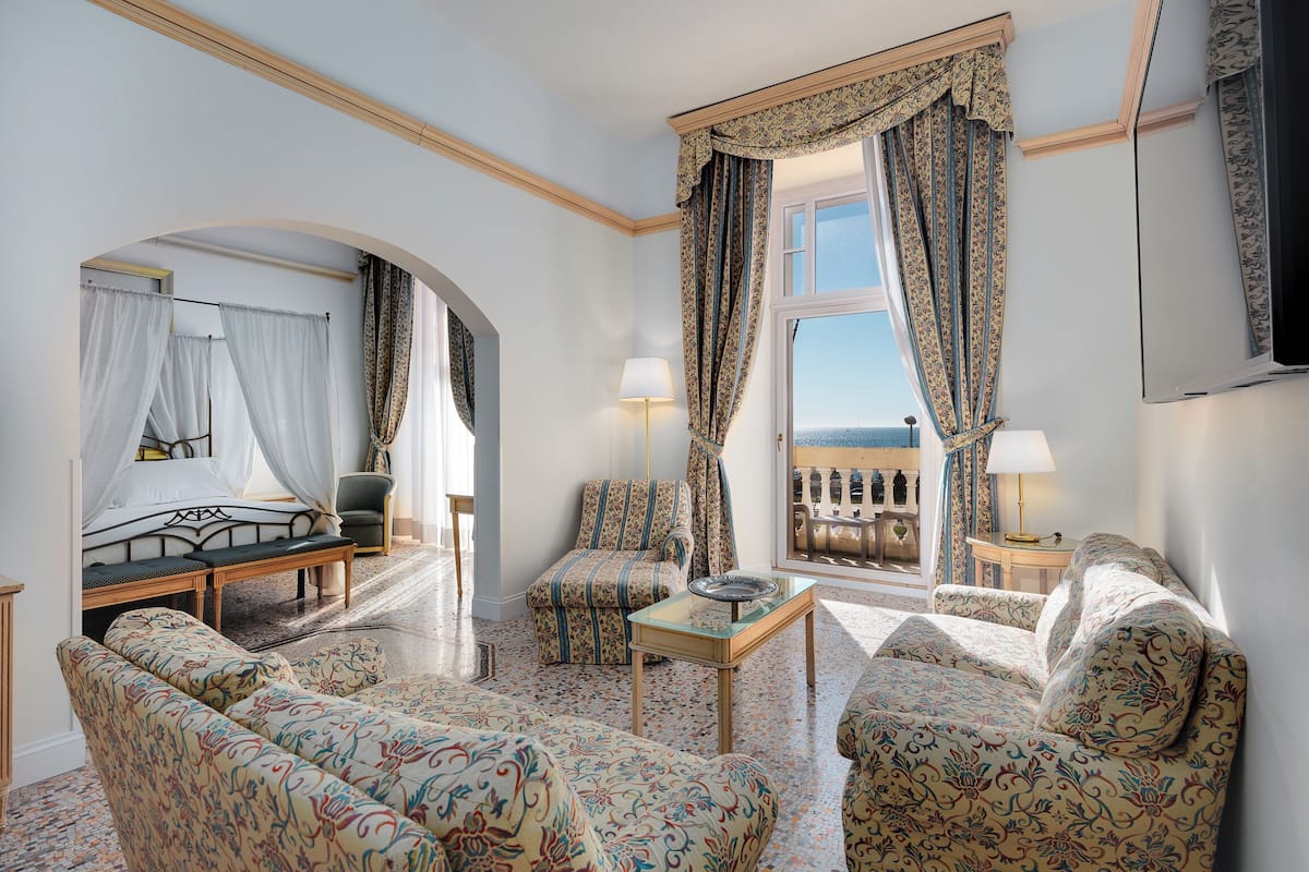 Een hotelkamer met een bed, een bank, een stoel, een tafel en een balkon met gordijnen.