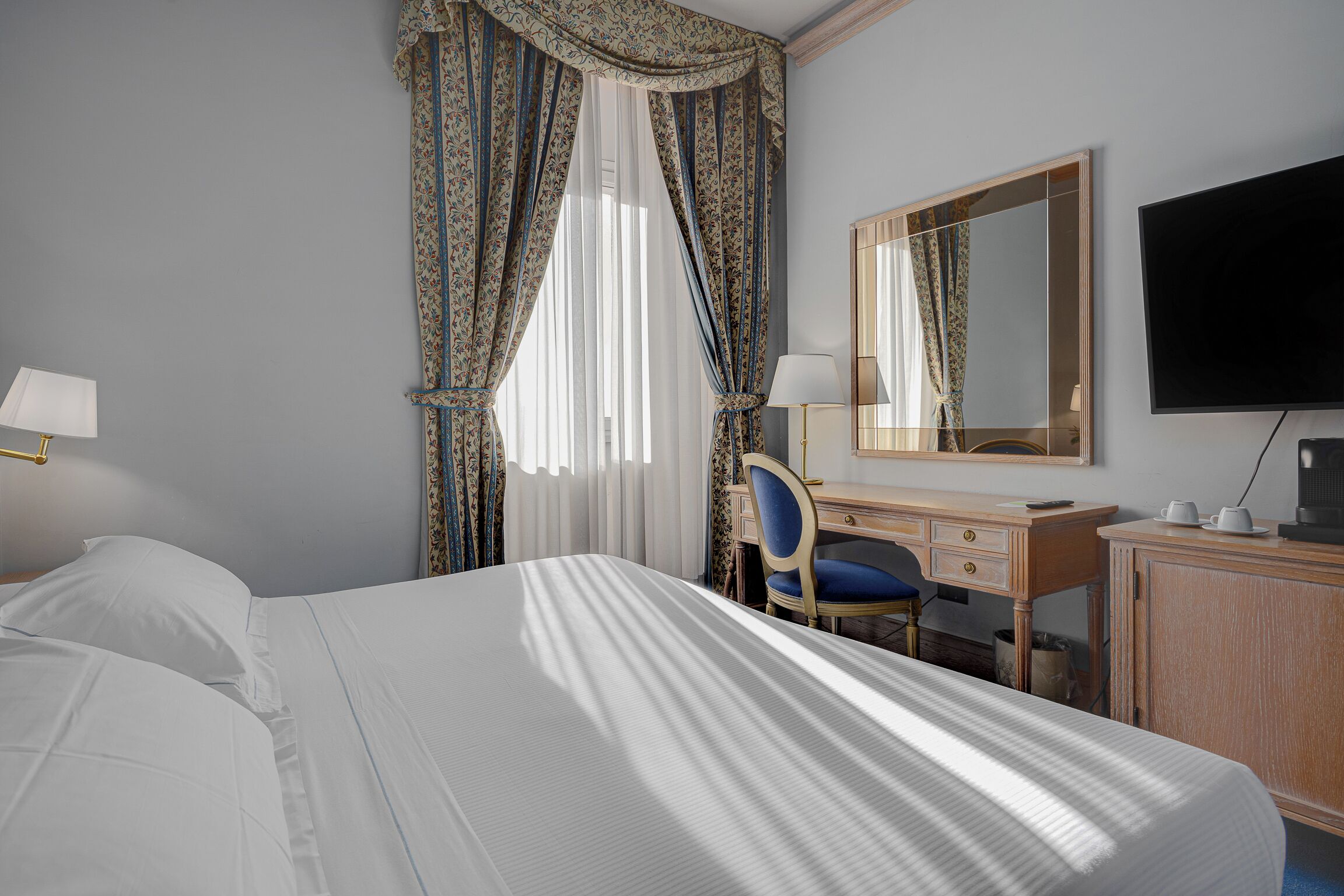 A hotel room with a large bed, a desk with a chair, a television, and a mirror.
