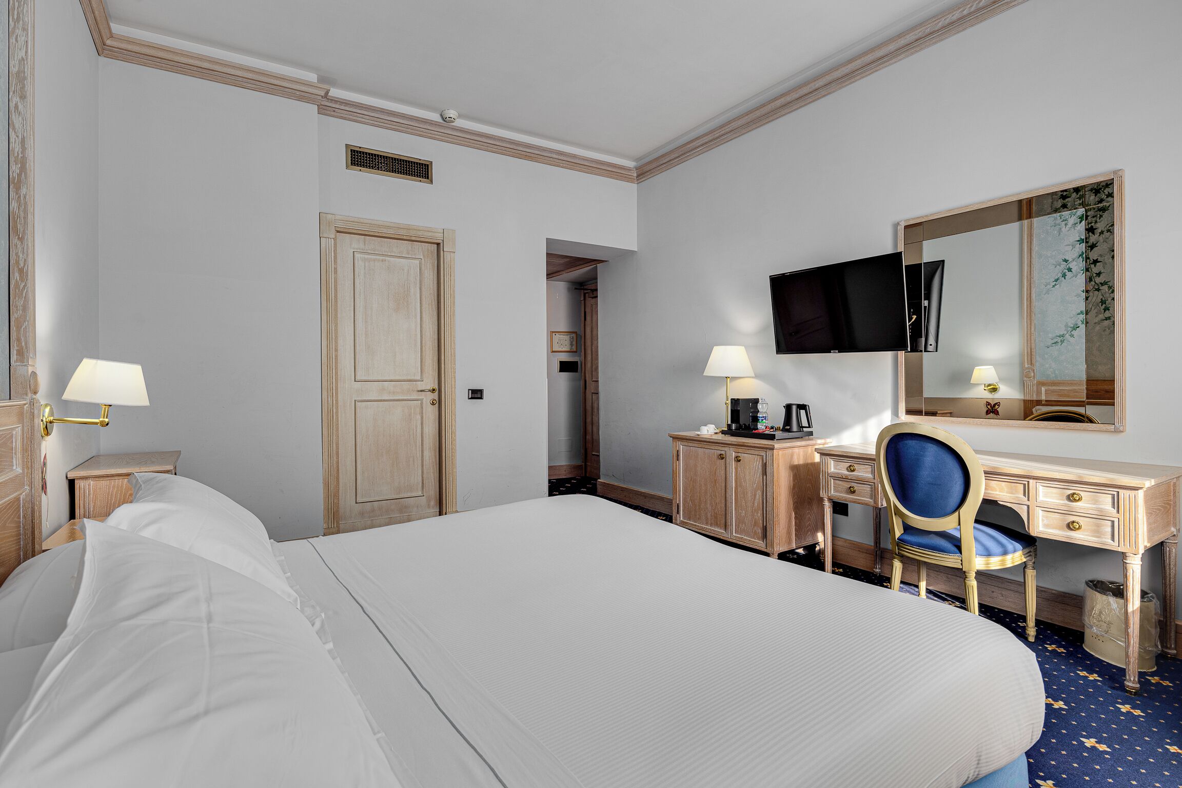A hotel room with a large bed, a desk with a chair, a television, and a mirror.