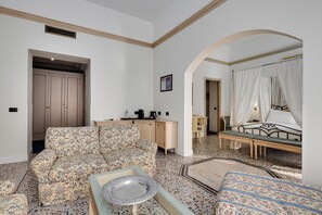 A spacious living room with a patterned sofa, a small table, and a bed with a canopy.