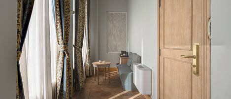Un pasillo con cortinas estampadas, una puerta de madera, un radiador y una mesita con una silla.