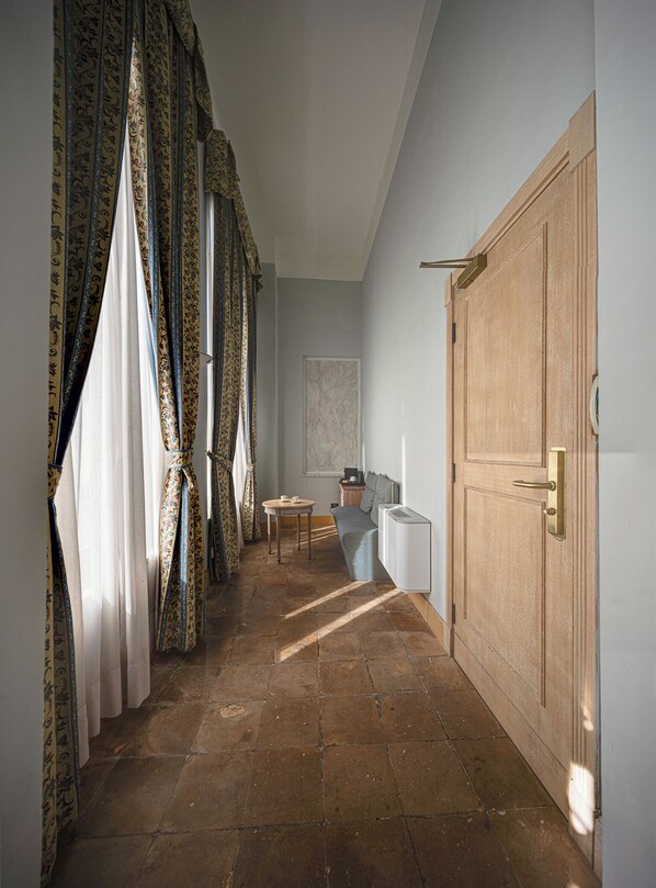 A hallway with patterned curtains, a wooden door, a radiator, and a small table with a chair. - Hotel de La Ville (Civitavecchia)