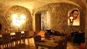 A dining area with stone walls, a table set for two, and a sofa.