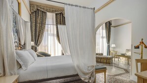 A bed with a canopy, a bedside table, a chair, a small table, and a mirror.