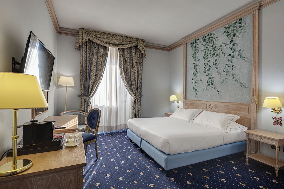 Een hotelkamer met een bed, bureau, stoel en een groot wandschilderij.