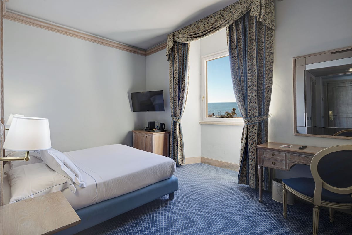 Een hotelkamer met een bed, bureau, stoel, televisie en een raam met gordijnen.