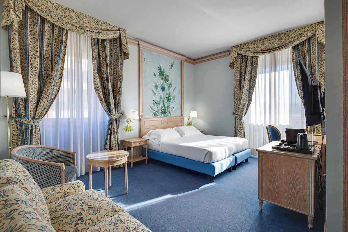 Een hotelkamer met een bed, een bureau, een stoel, een klein tafeltje en een schilderij aan de muur.