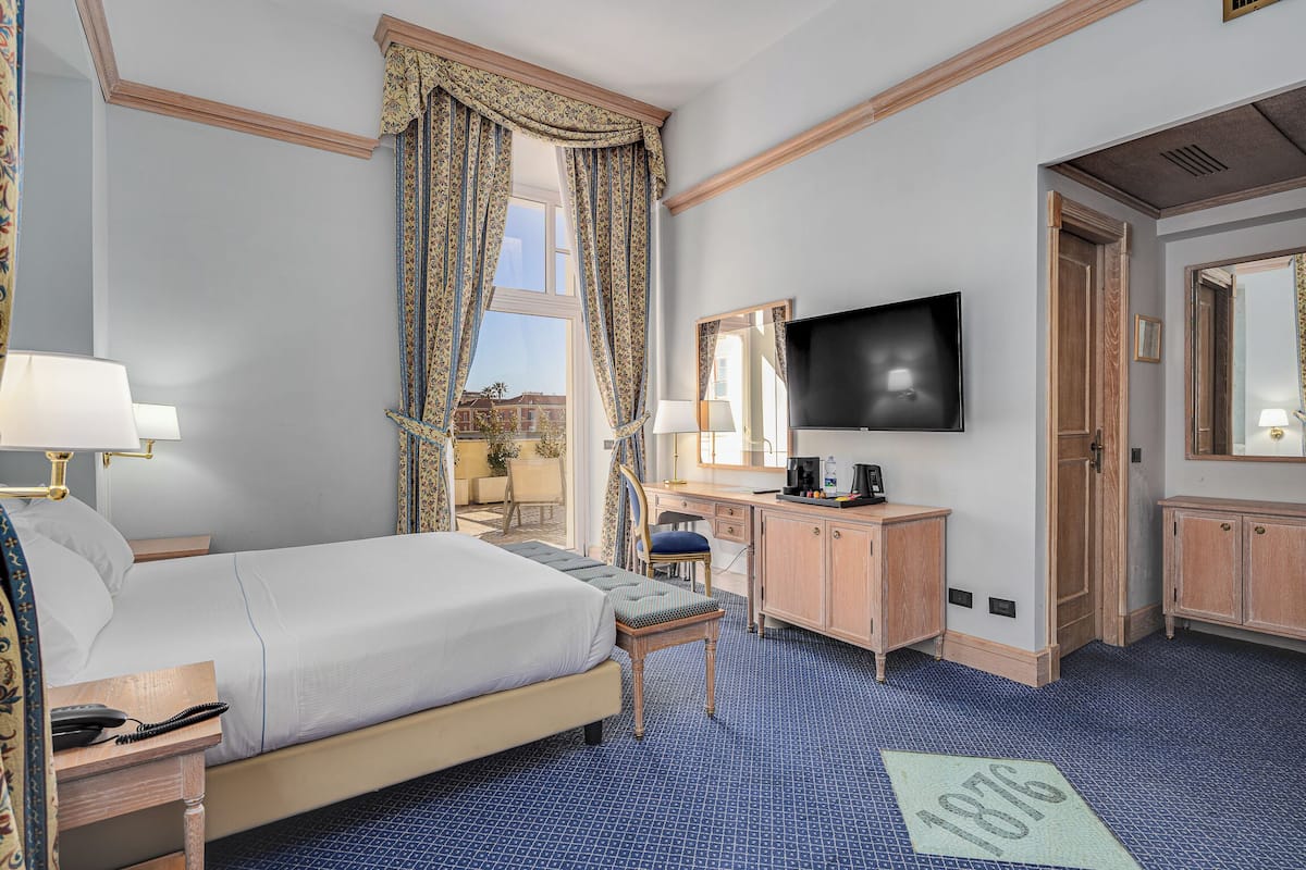 Hotelkamer met bed, bureau, stoel, televisie en uitzicht op de stad.
