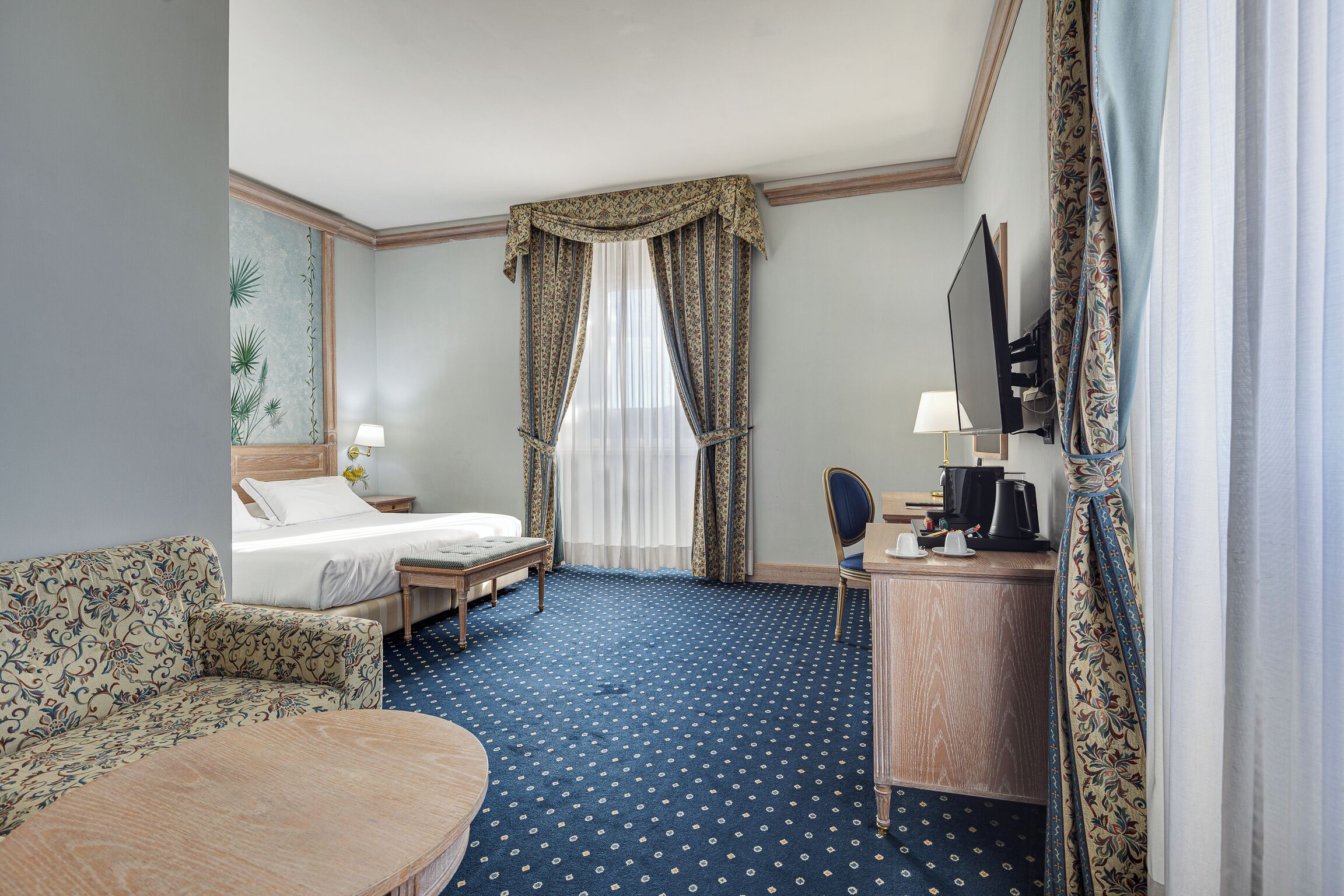 Ein Hotelzimmer mit Bett, Schreibtisch, Stuhl, Sofa und Fernseher.