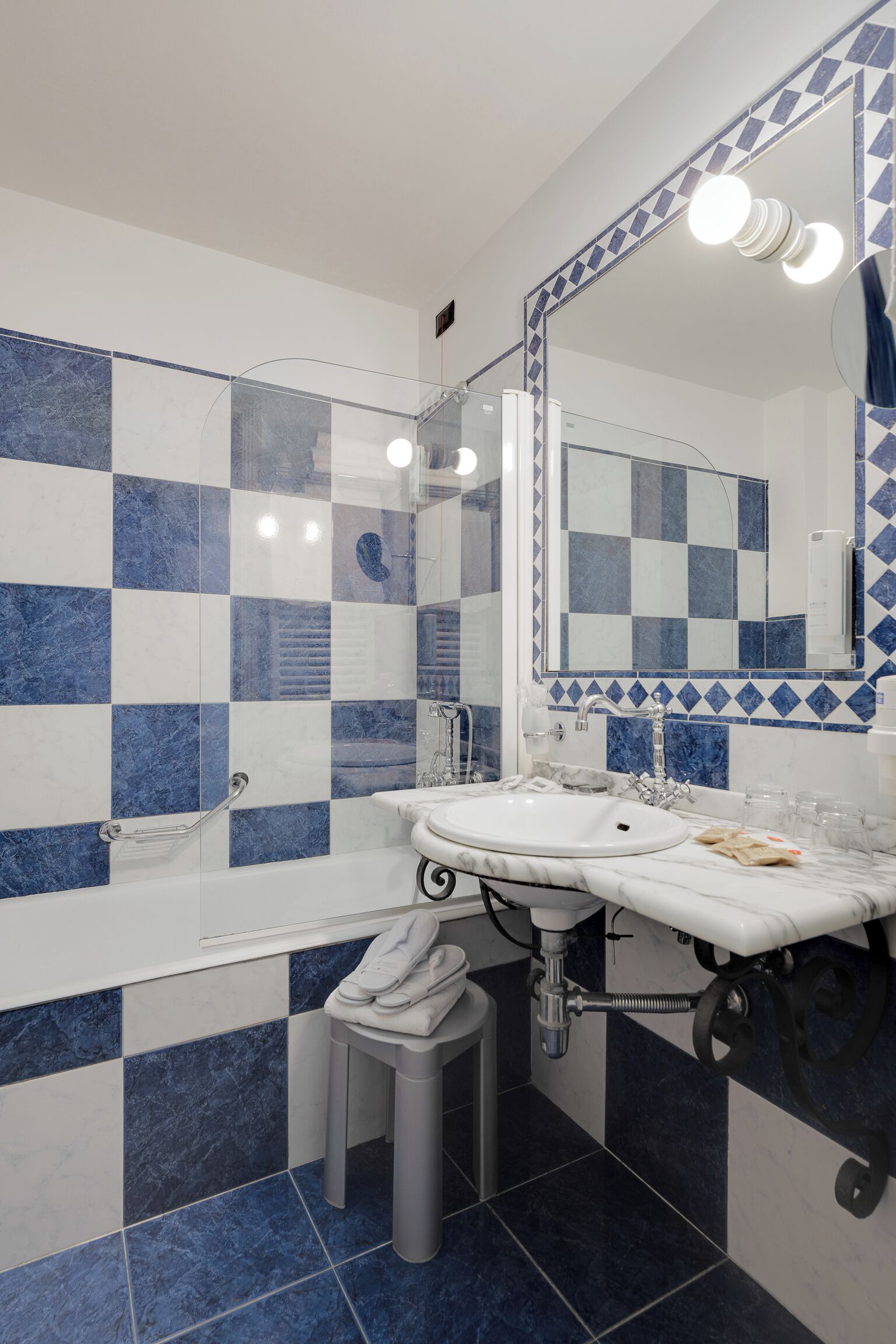 Un baño con piso de baldosas a cuadros, un lavamanos blanco, un espejo y un perchero para toallas.