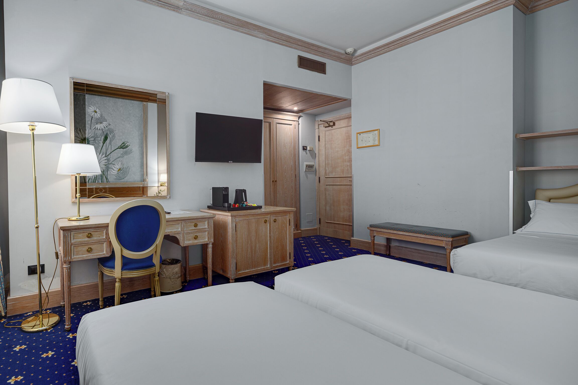 A hotel room with two beds, a desk with a chair, a television, a wardrobe, and a small table.