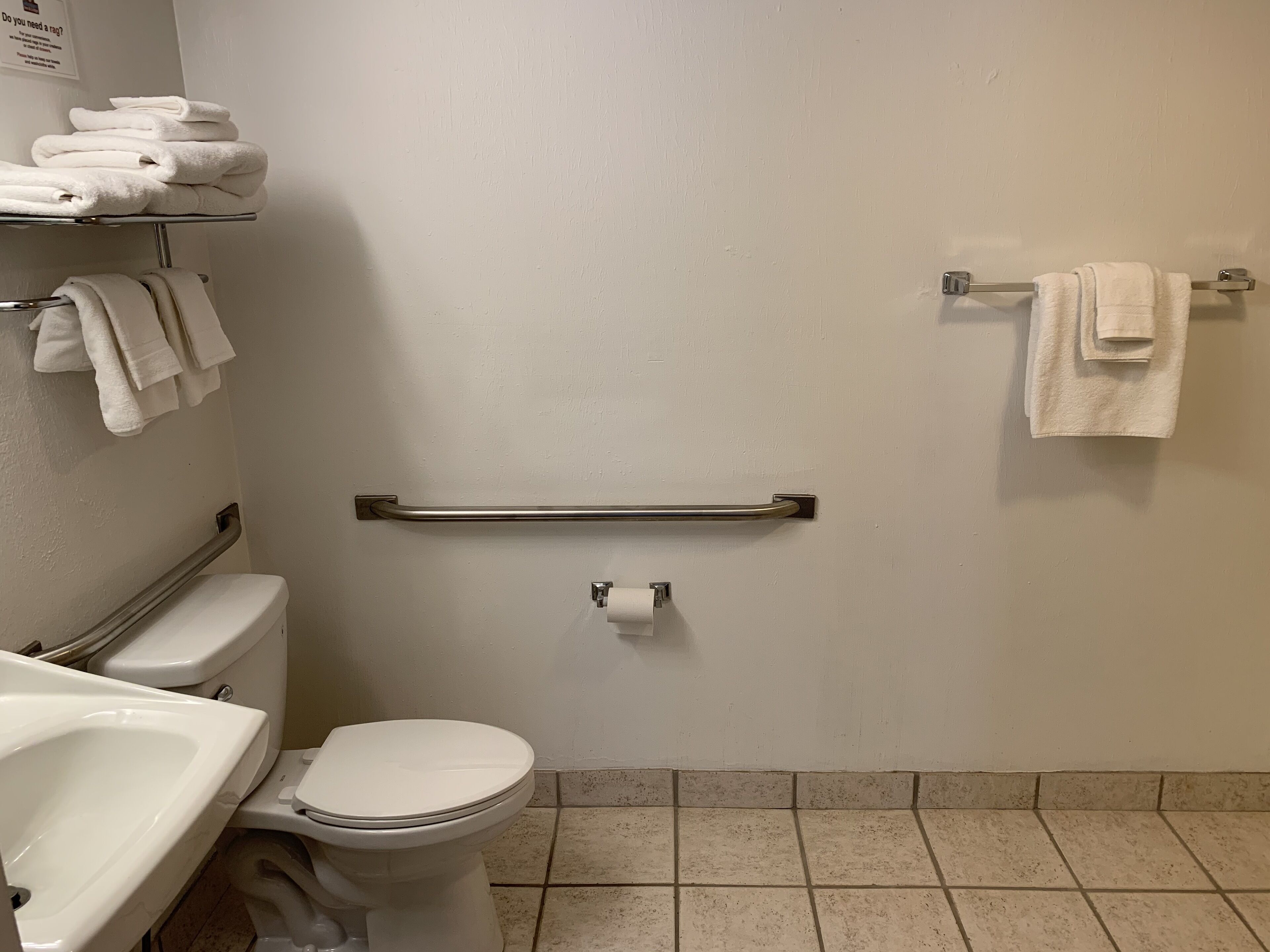 Une salle de bain équipée de toilettes, d’un lavabo et de barres d’appui.