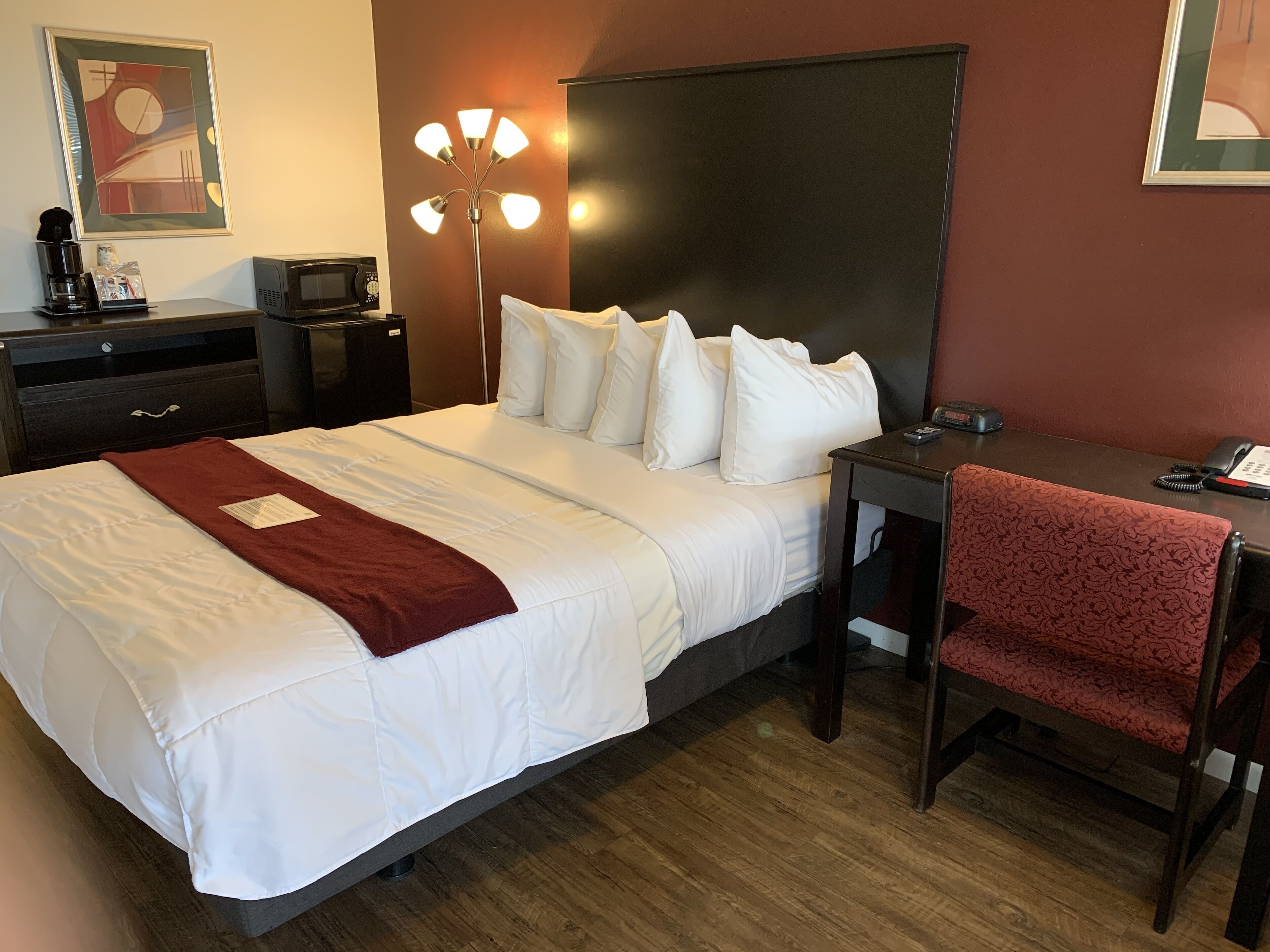 A hotel room with a large bed, a desk, a chair, a desk lamp, a coffee maker, a microwave, and a telephone.