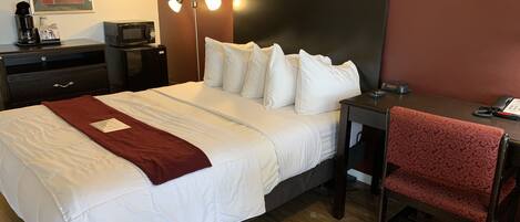 A hotel room with a large bed, a desk, a chair, a desk lamp, a coffee maker, a microwave, and a telephone.