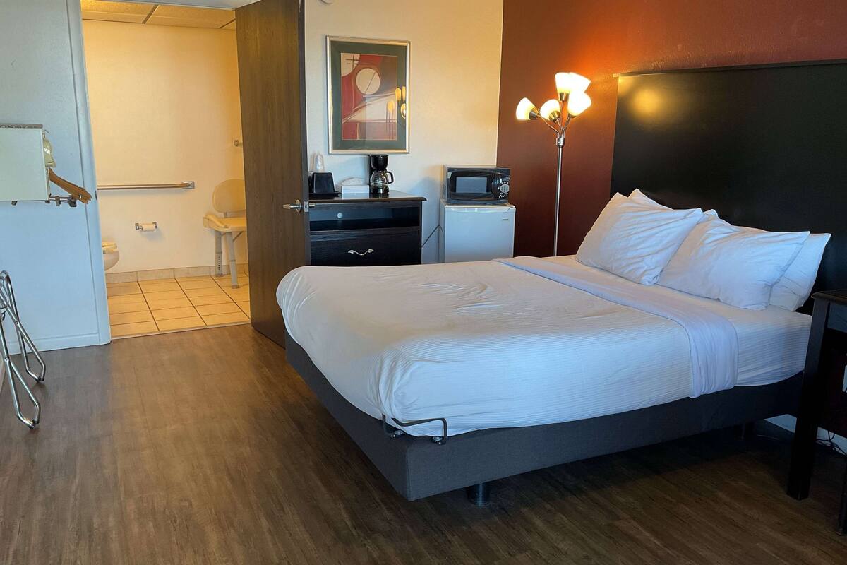 A hotel room with a bed, bedside tables, a desk, a chair, a microwave, a coffee maker, a telephone, and a toilet.