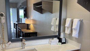 Ein Badezimmer mit großem Spiegel, Waschbecken, Handtuchhalter und Mülleimer.
