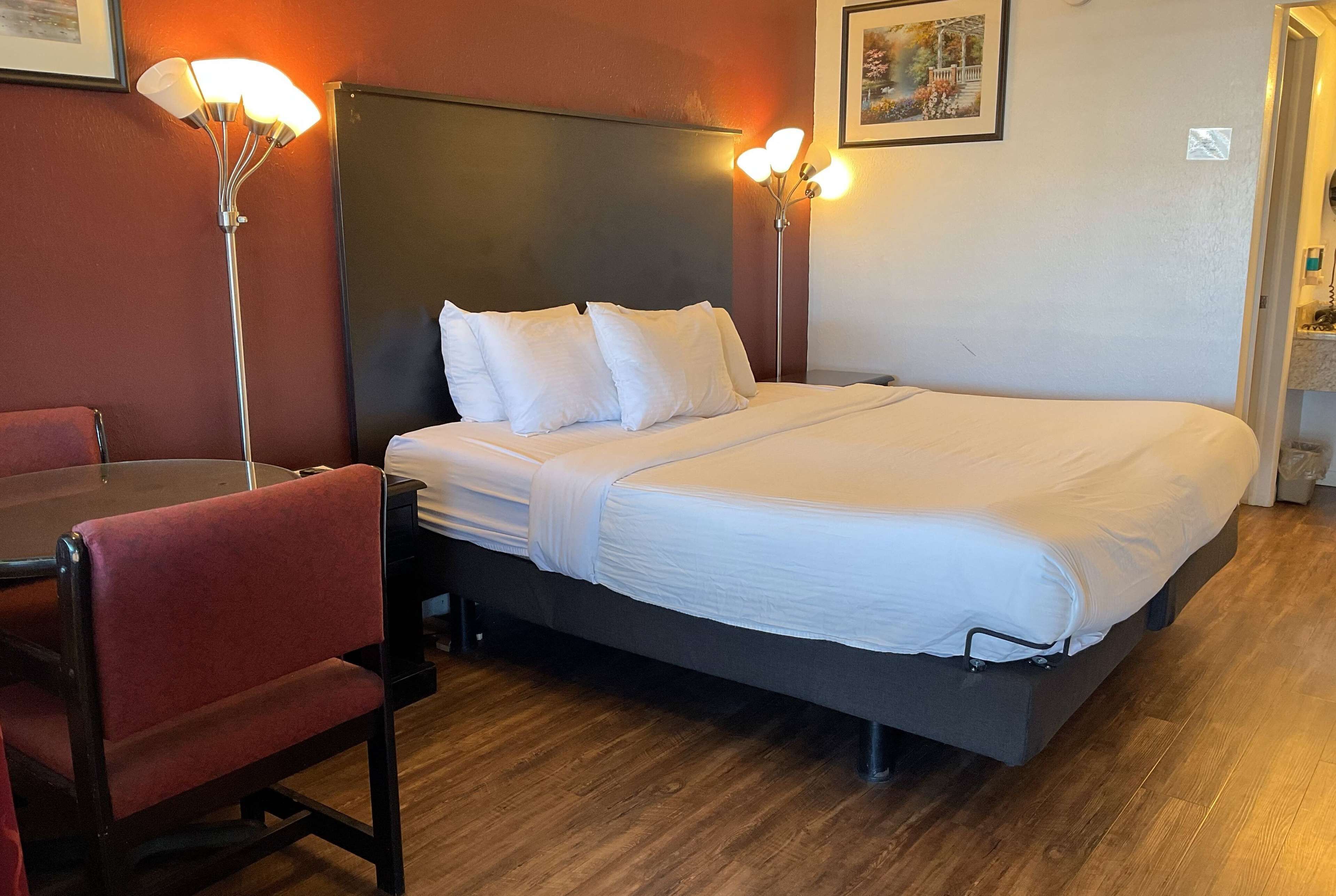 Quarto de hotel com uma cama grande, uma escrivaninha com cadeira e duas luminárias de cabeceira.