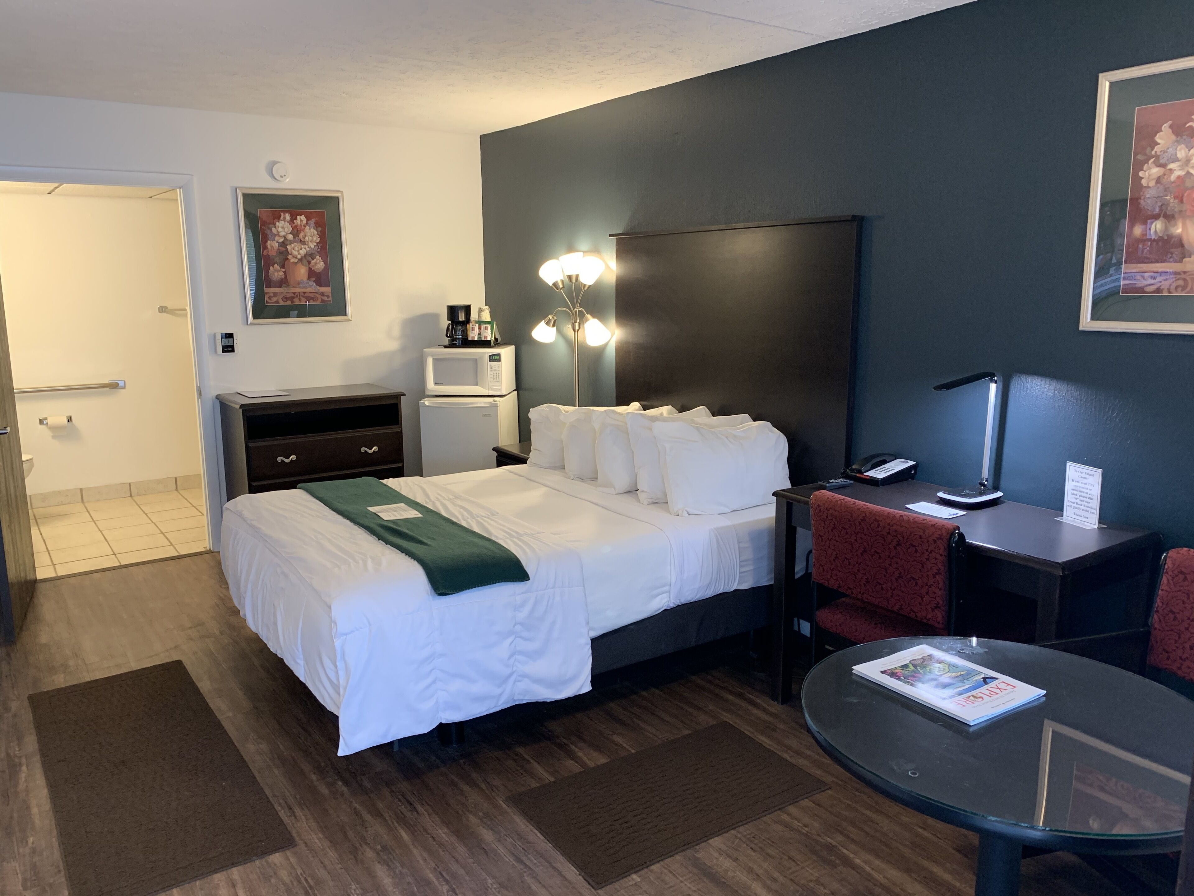 Una camera d'albergo con un letto, un comodino, una lampada e un tavolino con una rivista.