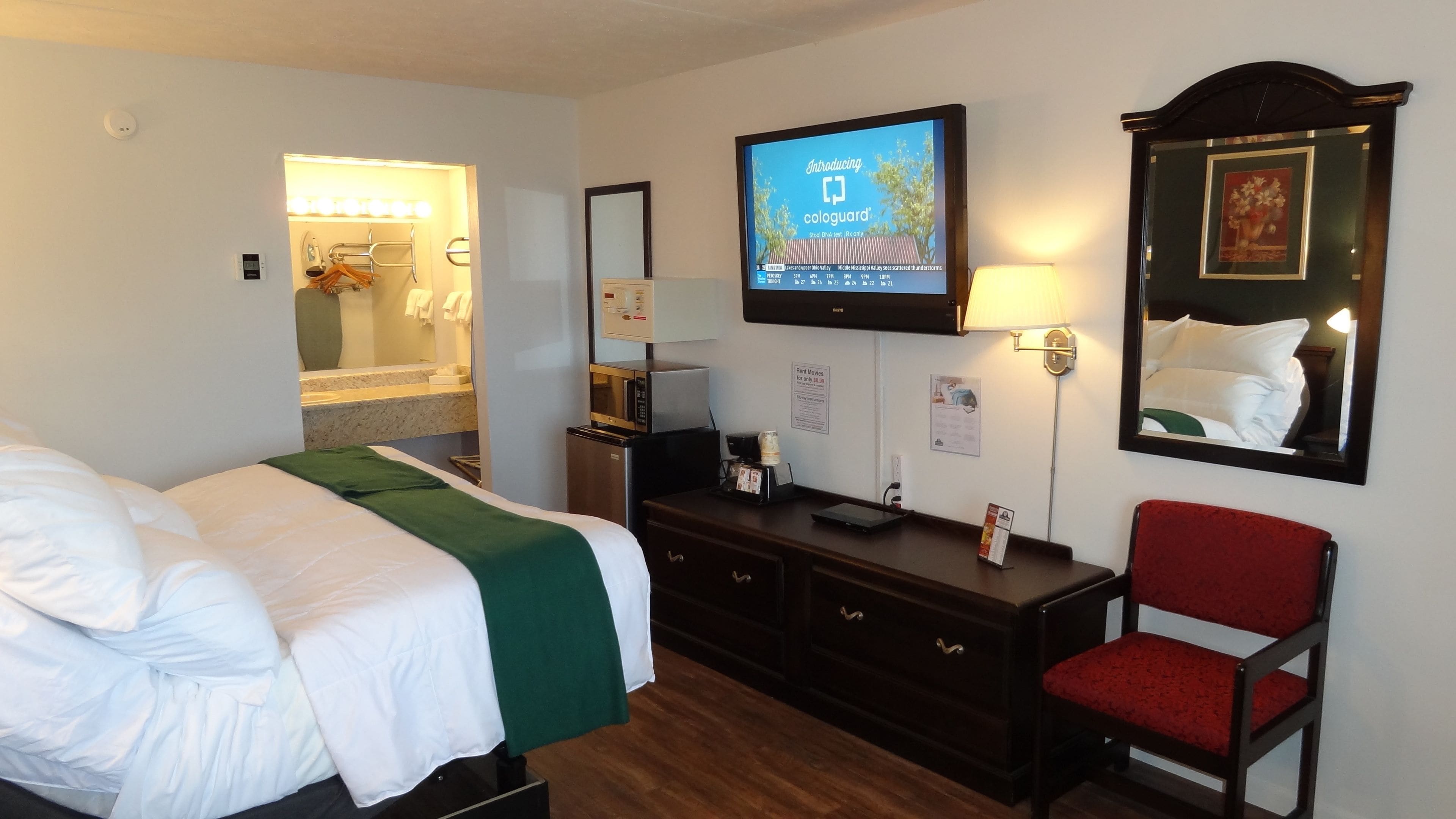 Una habitación de hotel con cama, televisión, escritorio, silla y espejo.