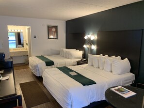 A hotel room with two beds, a desk, a chair, a small table, a lamp, and a framed picture on the wall.