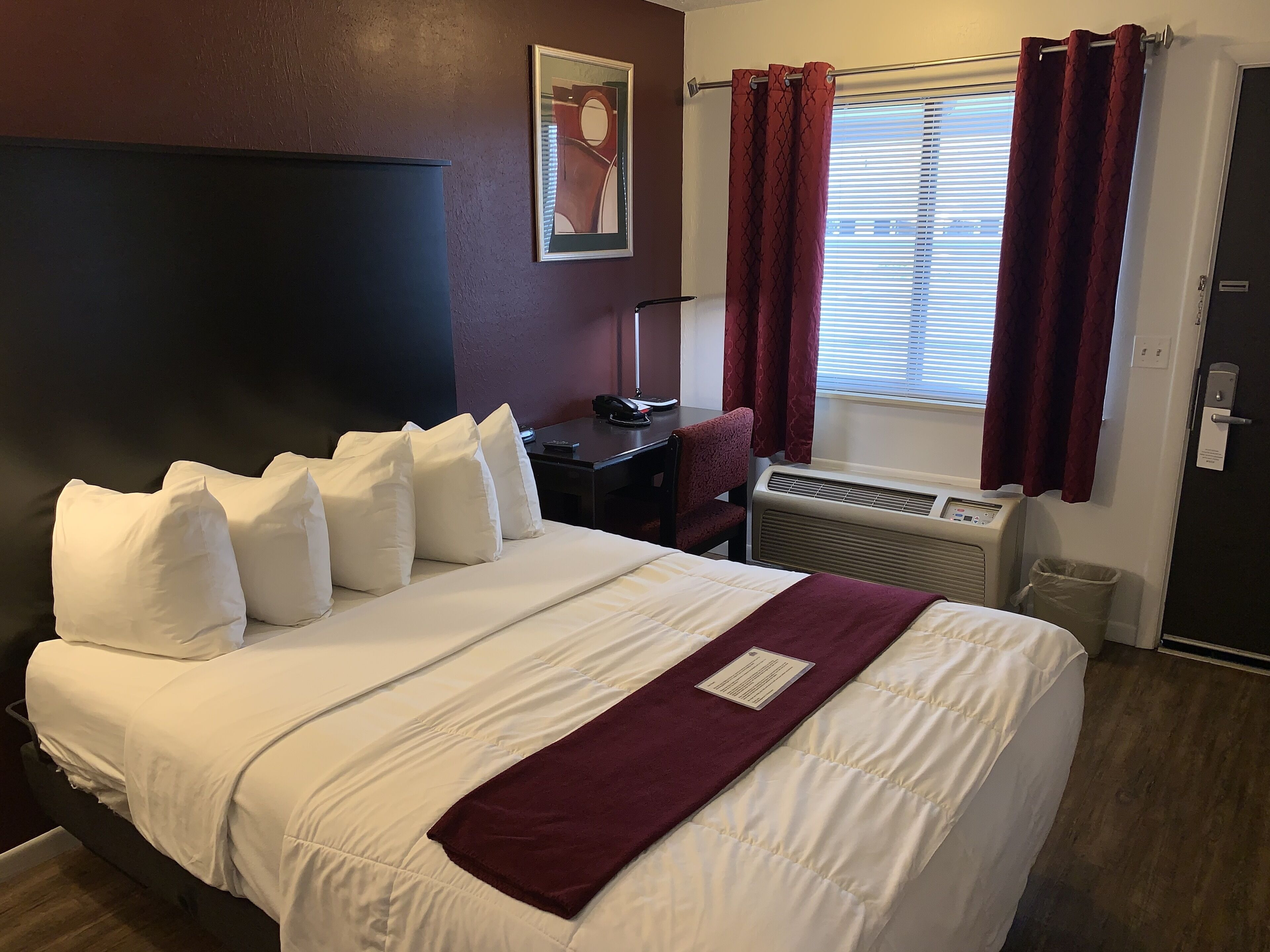 Een hotelkamer met een groot bed, een bureau, een stoel, een heater en een raam met gordijnen.