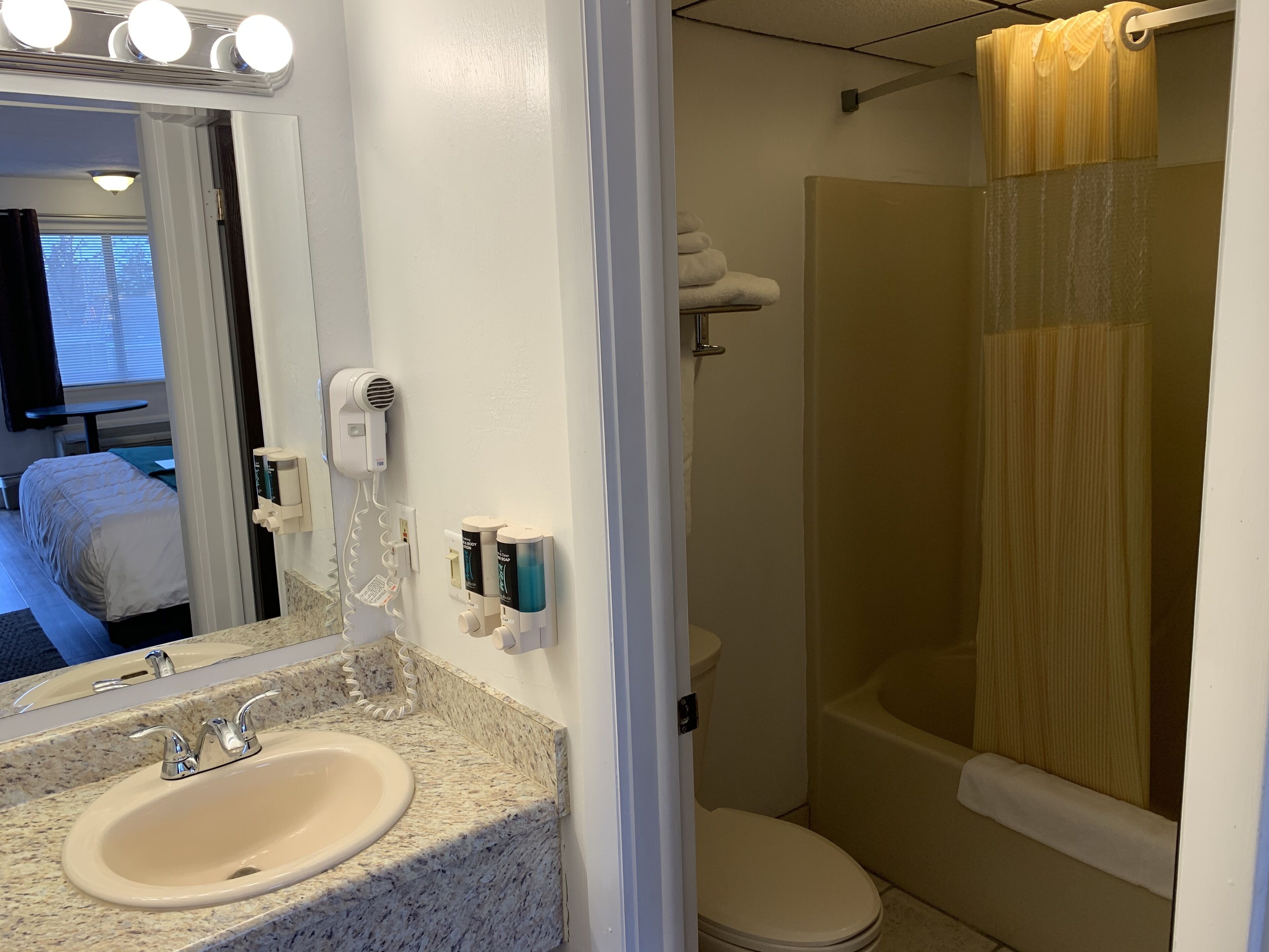 A bathroom with a sink, mirror, hairdryer, and shower curtain.