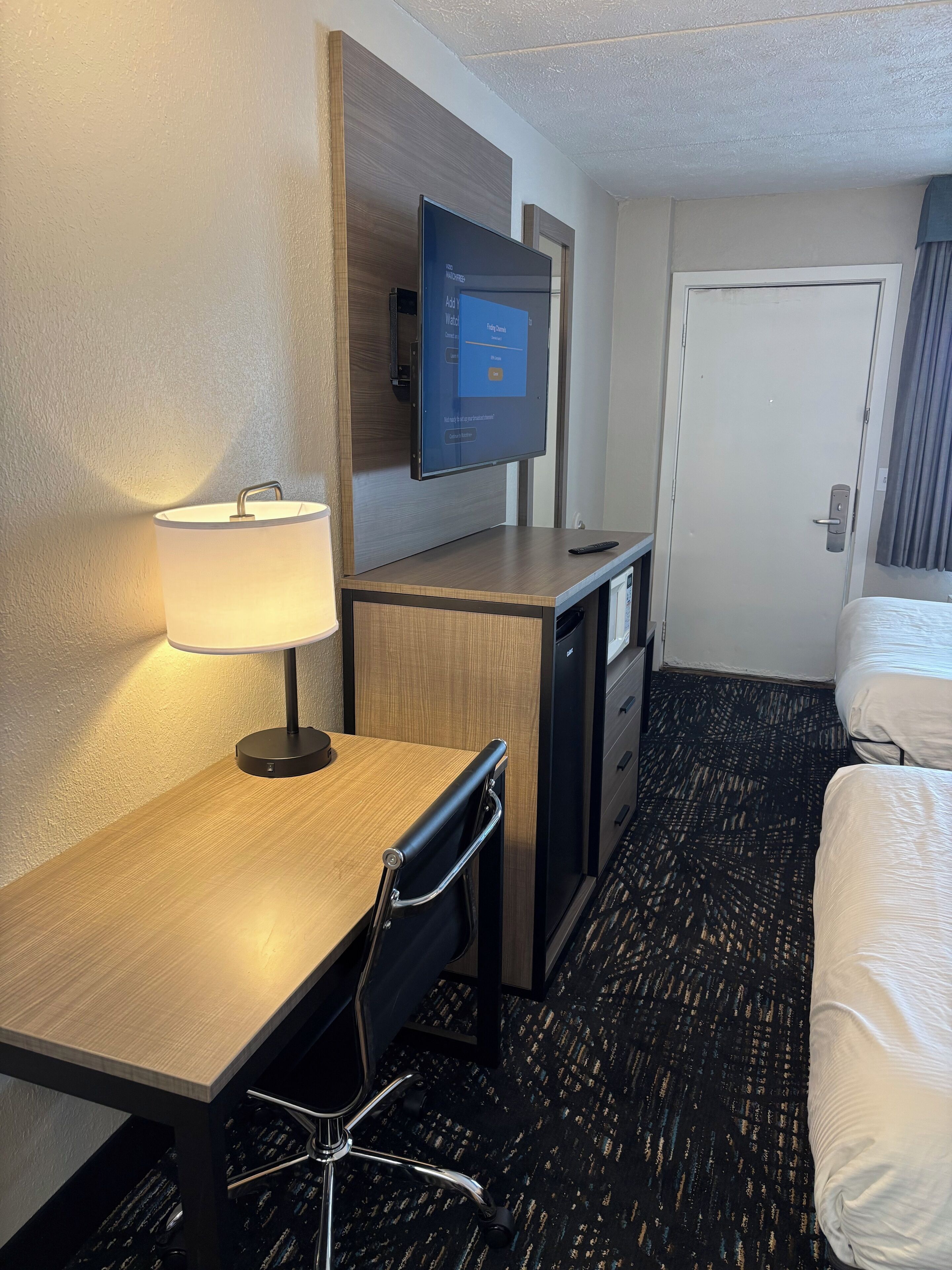 Una habitación de hotel con escritorio, silla, televisión, cama y puerta.