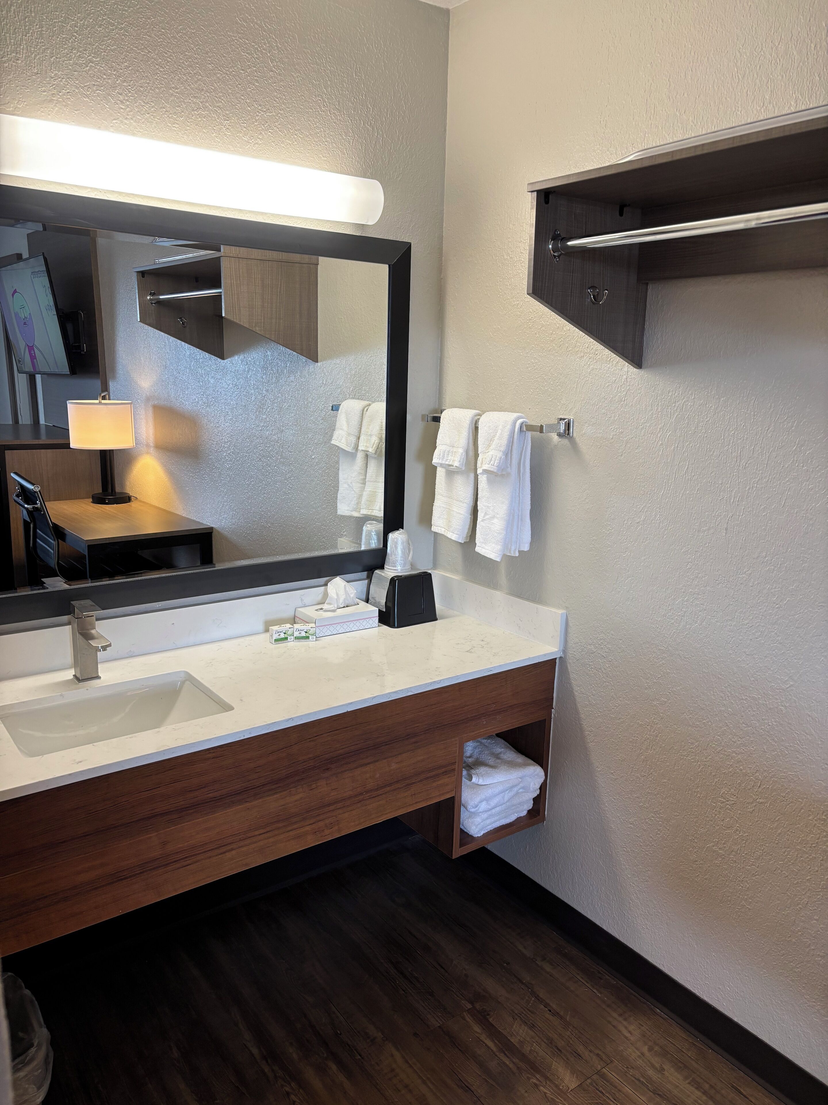A modern bathroom with a large mirror, a sink, a towel rack, and a shelf with toiletries.
