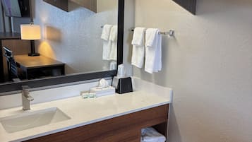 A modern bathroom with a large mirror, a sink, a towel rack, and a shelf with toiletries.