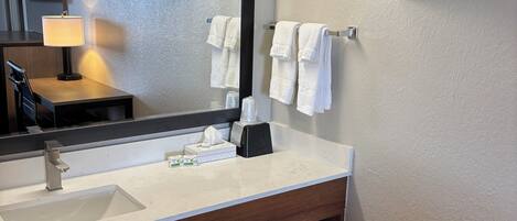 A modern bathroom with a large mirror, a sink, a towel rack, and a shelf with toiletries.