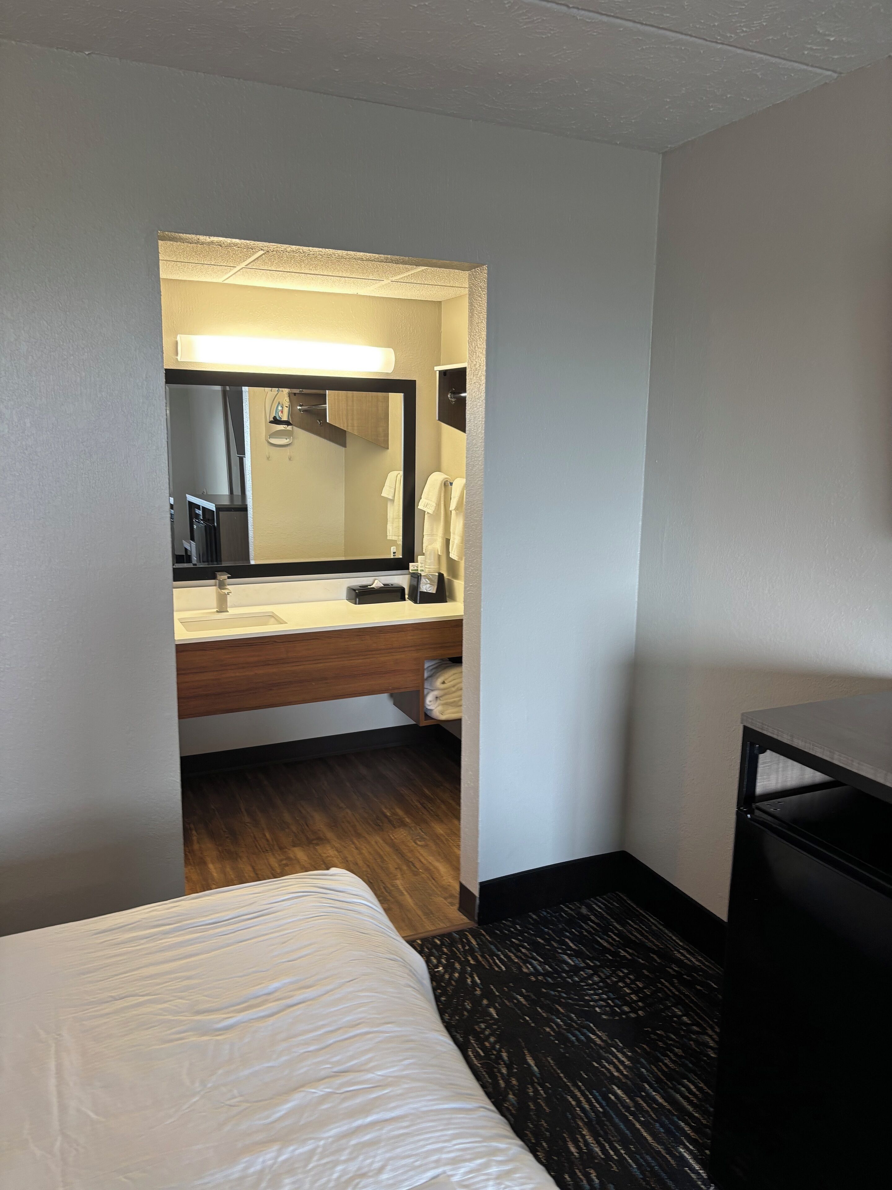 A hotel room with a bed, a bathroom with a sink, mirror, and towels, and a small desk.