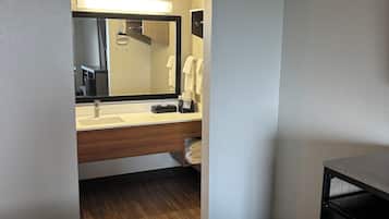 A hotel room with a bed, a bathroom with a sink, mirror, and towels, and a small desk.