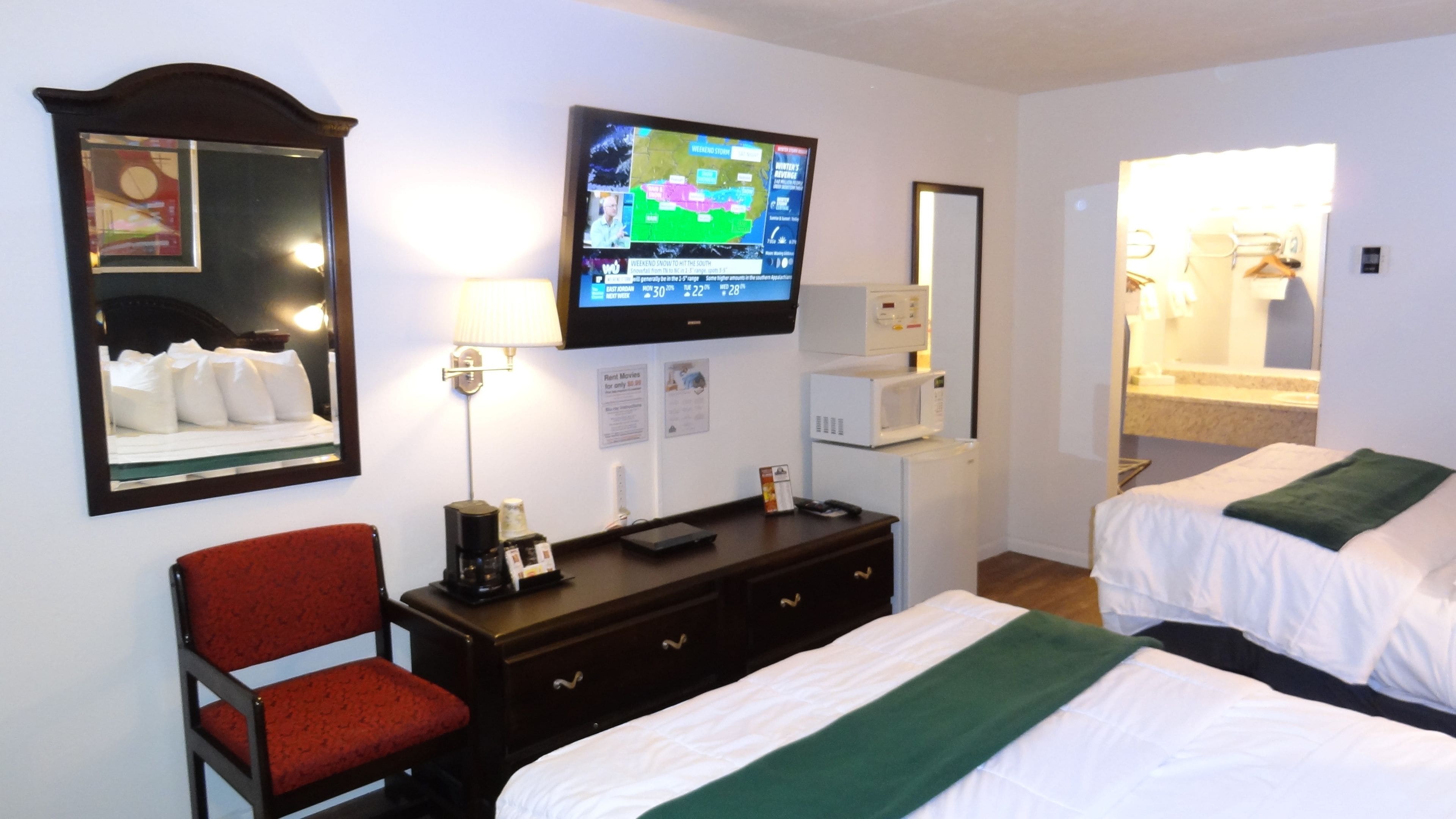Habitació d'hotel amb dos llits, una televisió penjada a la paret, escriptori amb una làmpada, una cadira i un mirall.