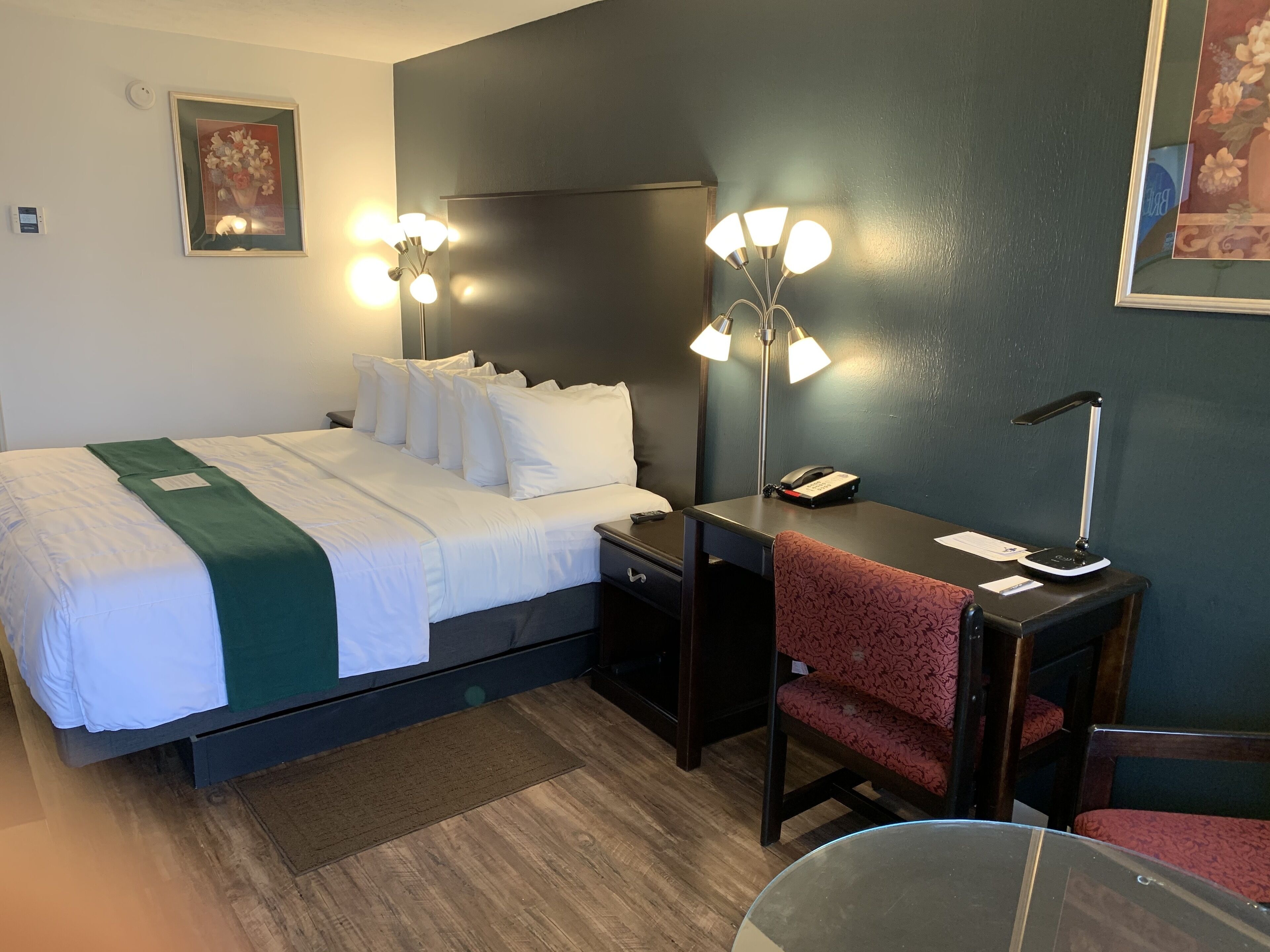 A hotel room with a bed, bedside table, desk, chair, and a desk lamp.