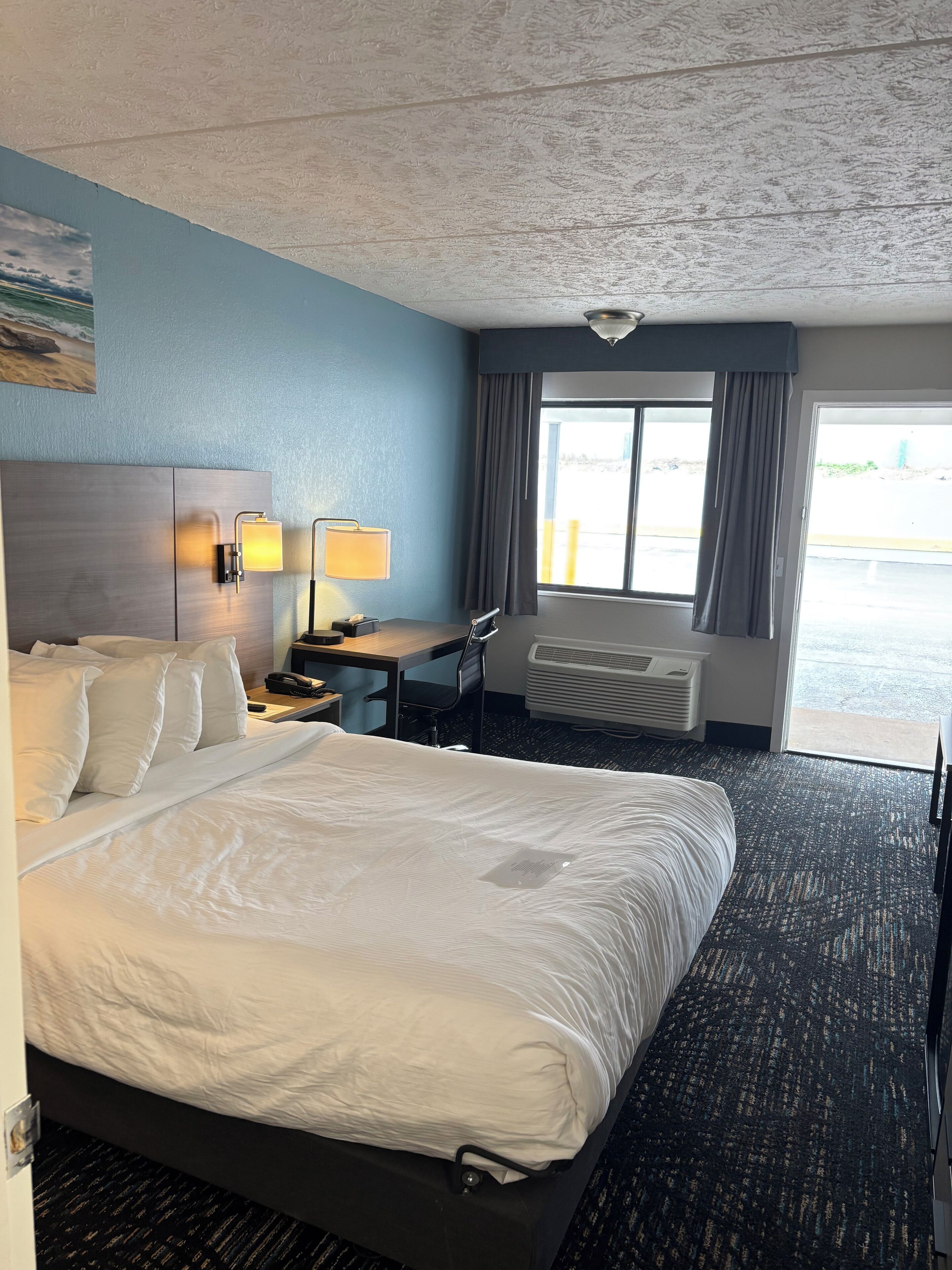 A hotel room with a bed, desk, chair, and a large window.