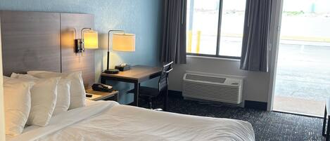 A hotel room with a bed, desk, chair, and a large window.