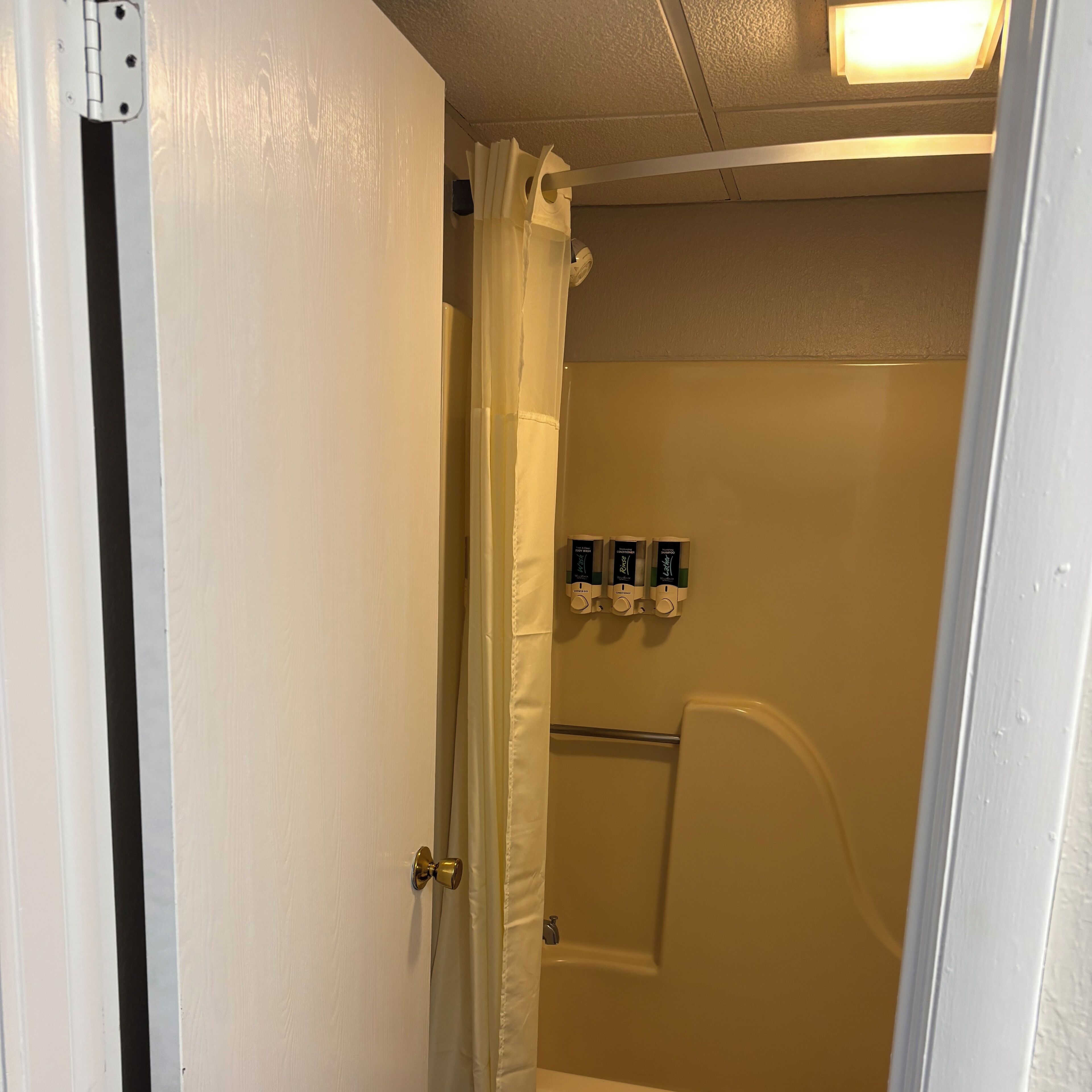 A bathroom with a shower, a towel rack with toiletries, and a door with a black stripe.