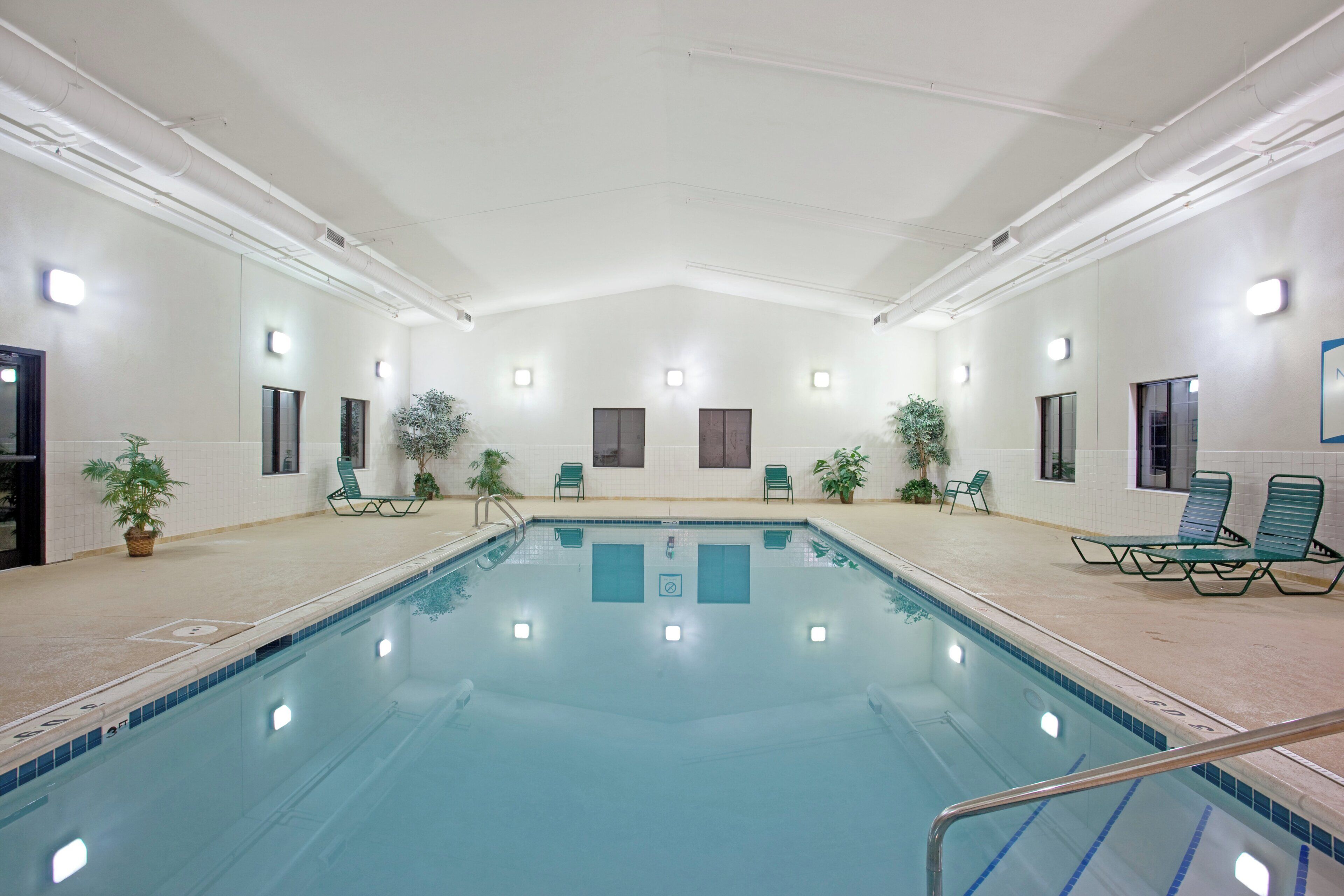 Una piscina interior con agua cristalina, rodeada de sillones de descanso y plantas en macetas.