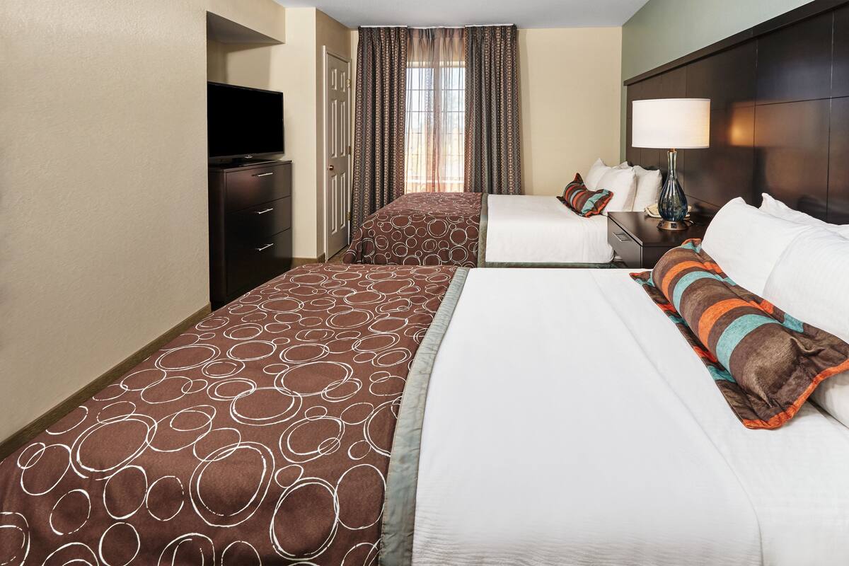 A hotel room with two beds, a TV, a desk, and a lamp.