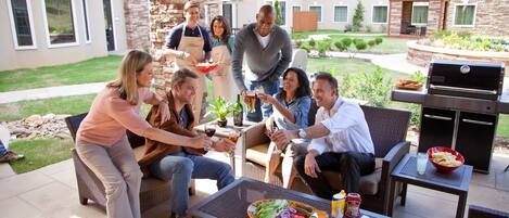 A group of people enjoying a meal outdoors with a grill and dining area.