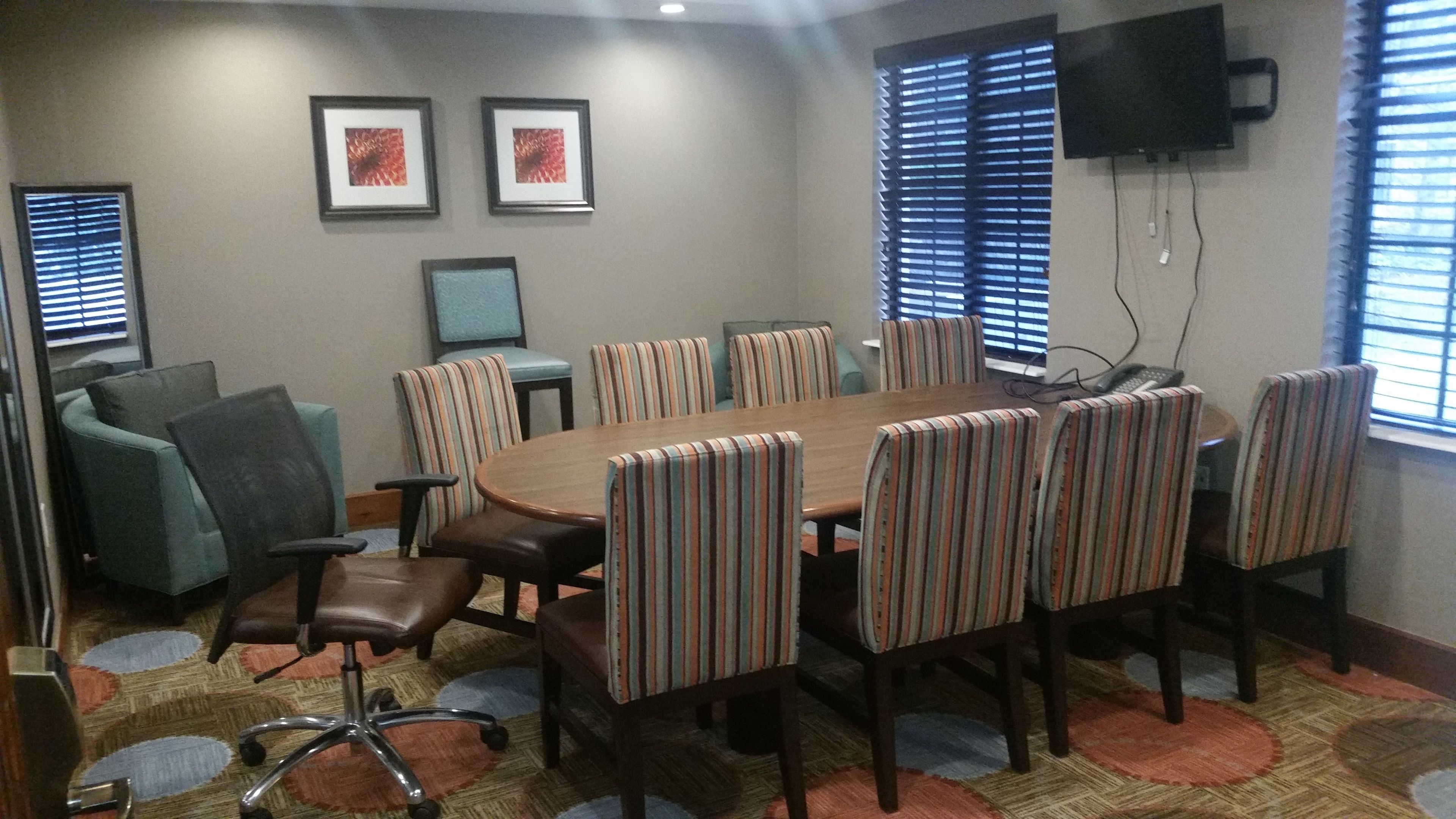 A conference room with a round table, striped chairs, a sofa, and a TV on the wall.