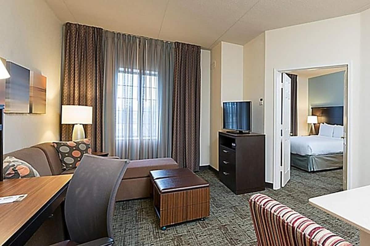 A hotel room with a sofa, a small table, a TV, a bed, and a bathroom visible through an open door.