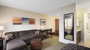 Ein Hotelzimmer mit einer Couch, einem Hocker, einem Schreibtisch, einem Stuhl und einem großen Spiegel.
